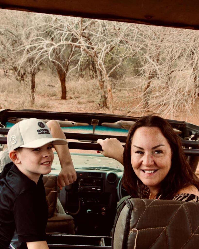 A woman and a girl in a safari jeep, turned around to look towards the camera, smiling.