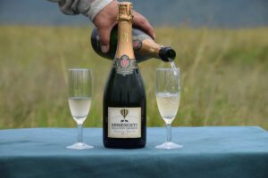 A close-up of a bottle of champagne with the flutes next to it. A hand is pouring champagne from a second bottle into one of the glasses.