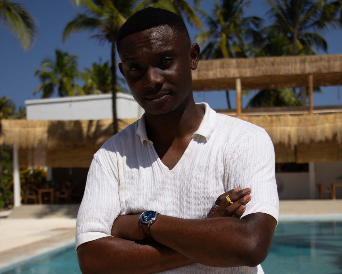 A close-up of a black man wearing a white shirt, looking towards the camera.